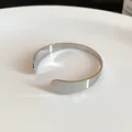 Close-up of a minimalist silver-colored metal open cuff bracelet on a smooth white surface. - Liquid Metal Minimalist Style / Silver