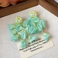 Close-up of mint green chiffon flower earrings with pearls and bead embroidery detail - Green