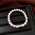 Primo piano di un bracciale di perle di lusso con ciondolo a fiocco in zircone dorato. - Rosa Chiaro