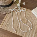 Dettaglio di orecchini a fiocco con perline in stile francese su un tappeto di paglia. - Bianco perla