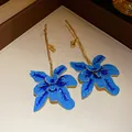 Dettaglio di orecchini a fiore in smalto blu artistico con steli dorati a ramo - Forma di Orchidea (HE32833) / Blu