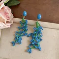 Close-up of elegant blue and green floral beaded dangle earrings on a textured background - Silver Earring Post Style / Blue Green