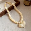Dettaglio di una collana in acrilico crema con perline cilindriche e grande ciondolo a cuore. - Beige