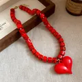 Primo piano di una collana di perline in acrilico rosso con ciondolo a cuore lucido. - Rosso