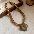 Vista dettagliata di una collana di perle acriliche ambra con un grande ciondolo a cuore - Caffè Scuro