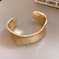 Detalle de un brazalete dorado abierto con una textura martillada y plisada única. - Bangle / Dorado