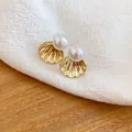 Elegant gold shell stud earrings with white pearls on a soft fabric background. - Gold