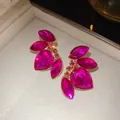 Detalle macro exquisito de pendientes de cristal rosa vibrante con diseño de pétalo dorado - Aguja de Plata Dorado Magenta