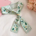 Detail view of a green floral print skinny silk scarf with a decorative yellow buckle - Green Floral