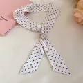 Close-up of blue polka dot skinny scarf featuring a silver four-leaf clover charm buckle - White Polka Dot