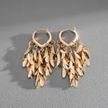 Detail shot of vintage style gold metallic leaf tassel hoop earrings on grey leather. - Silver Needle / Gold