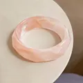 Macro detail of faceted acrylic bangle with peachy marble texture and high-gloss finish - Pink