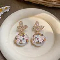Primo piano di orecchini a lobo a farfalla e fiori con dettagli in cristallo e perle - Stile Fiore Farfalla Strass (HE33405) / Oro-Perla Grigia