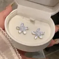 Exquisite silver-tone flower stud earrings with a sparkling crystal center in a white jewelry box - Flower Stud Earrings / White