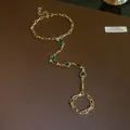 Detailed view of vintage gold hand chain bracelet with green heart and rectangular gems - Ring-Linked Bracelet / Gold / Green