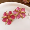 Gros plan détaillé de boucles d'oreilles fleur rose avec pétales dorés texturés - Boucles d'oreilles clous / Rose rouge