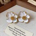 Gros plan détaillé sur des boucles d'oreilles fleurs en émail blanc avec pistils dorés - Blanc