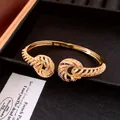 Detailed view of elegant 18K gold-plated open bangle featuring sparkling zircon-set twisted knots. - Bangle / Gold