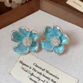 Gros plan de boucles d'oreilles clips fleurs en émail bleu sur fond décoratif vintage. - Bleu