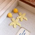 Close-up of yellow resin star flower earrings with marble texture on beige fabric. - Yellow