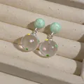 Detail view of clear resin earrings with colorful polka dots in a beige box. - Silver Earring Post Style / Green