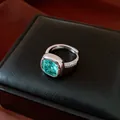 Détail d'une bague avec pierre verte taille coussin sur un écrin de bijoux noir chic - Anneau / Vert