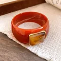 Close-up of reddish-brown acrylic bangle with square amber resin inlay and gold trim. - Orange And Coffee