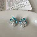 Close-up of elegant flower earrings with blue crystals and white pearls in a tray. - Flower Shape / Silver-Blue