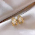 Dettaglio di eleganti orecchini a lobo a forma di C in oro con pavé di zirconi cubici - Oro