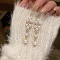 Close-up of elegant gold drop earrings with white pearls and zircon on soft white knitwear. - Gold-White
