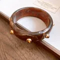 Detailansicht eines Retro-Armreifs aus marmoriertem Harz mit eleganten goldenen Nieten. - Dunkelbraun