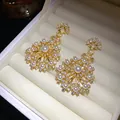 Gros plan détaillé de boucles d'oreilles fleurs en zircon et perles dans une boîte blanche. - Style Tige d'Oreille en Argent / Or