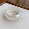 Detalle de un brazalete ancho transparente e iridiscente minimalista con un brillo vibrante aurora. - Blanco