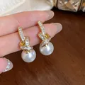 Close-up of elegant gold ribbon earrings with zircon crystals and round white pearls. - Ribbon Knot Pearl Pendant Style