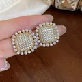 Macro view of square zircon stud earrings with small white pearls on a female hand. - Square Flower Style