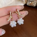 Elegant gold bow earrings with sparkling zircons and delicate white pearl clusters close-up - Bowknot Floral Style