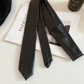 Close-up of a minimalist black faux leather necktie necklace on a lifestyle prop background - Black