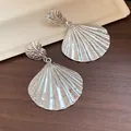 Detailed macro view of vintage silver metallic pleated shell drop earrings on wooden surface - Shell Pendant Style (HE33029) / Silver