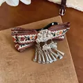 Detailed macro view of vintage Bohemian hair clip featuring floral ribbon and metal tassels - White