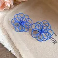 Detailed view of the intricate blue wire-wrapped hollow flower stud earrings on a tray - Blue