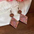 Close-up of bohemian pink diamond-shaped earrings with ethnic floral patterns and wood accents - Brown And Pink