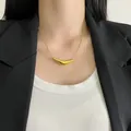 Detailed shot of a minimalist gold smile pendant necklace on a model wearing a blazer. - Gold