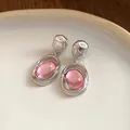 Close-up shot of elegant retro pink acrylic oval pendant earrings resting on a white ceramic plate - Pink