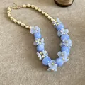 Gros plan d'un collier de fleurs bleues avec perles dorées et finition élégante mate - Or-Bleu