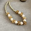 Gros plan d'un collier de fleurs élégant avec des perles crème et des pétales d'ambre. - Brun doré