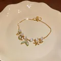 Close-up detail of starfish and fishtail charms with opal beads on gold bracelet - Gold