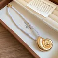 Close-up of golden conch shell pendant on white silky rope necklace in jewelry box - Glossy Style / Gold