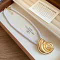 Macro view of a golden metal conch pendant on a braided white silk rope necklace in a box - Matte Finish / Gold