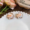 Detailed view of warm-toned camellia stud earrings on a decorative white plate - Camellia Stud Earrings (HE32634) / Silver Needle / Pink