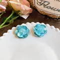 Detail view of light blue camellia flower stud earrings on a white plate - Camellia Stud Earrings (HE32634) / Silver Needle / Blue